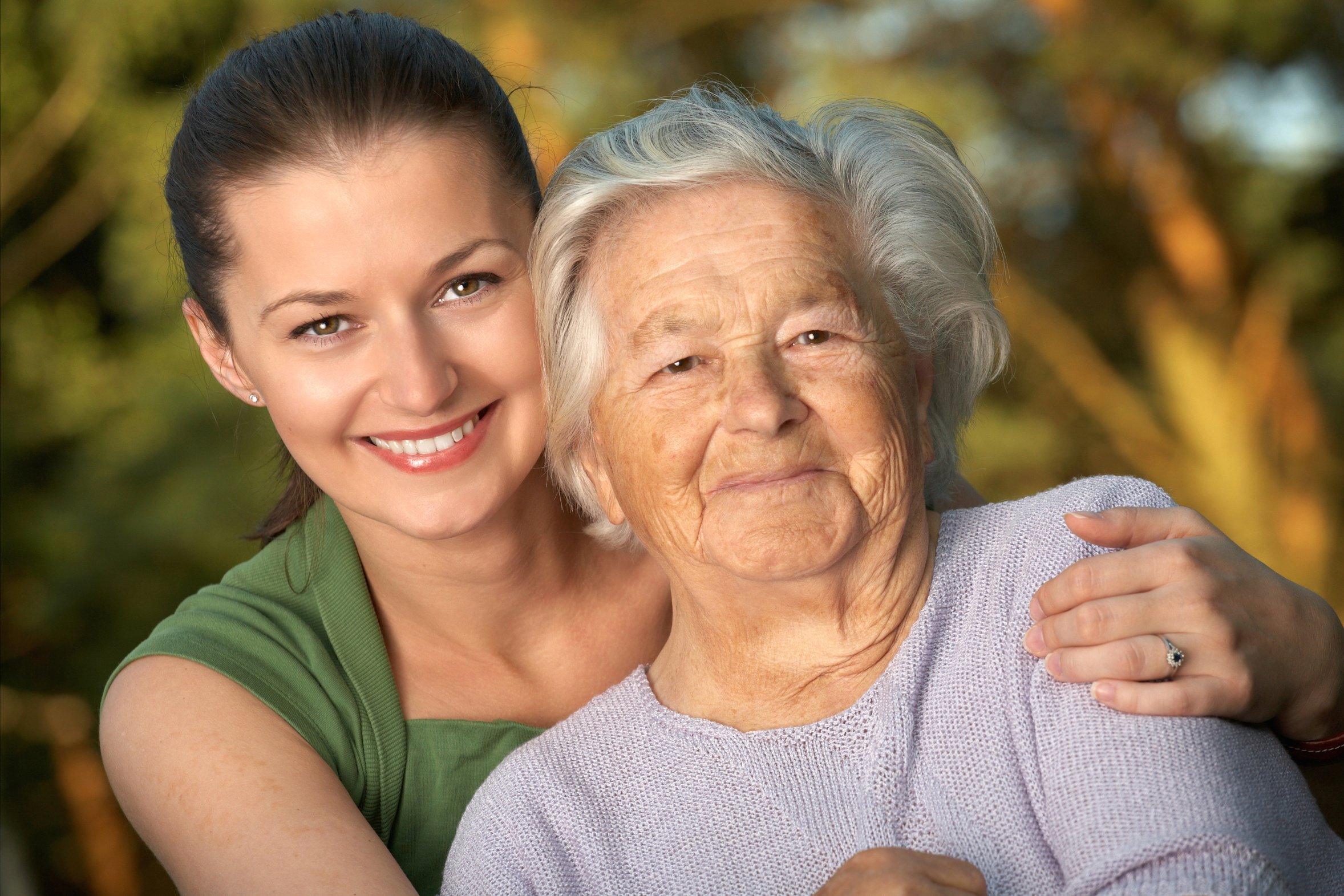 Betreuungskraft und Seniorin Wange an Wange im Freien