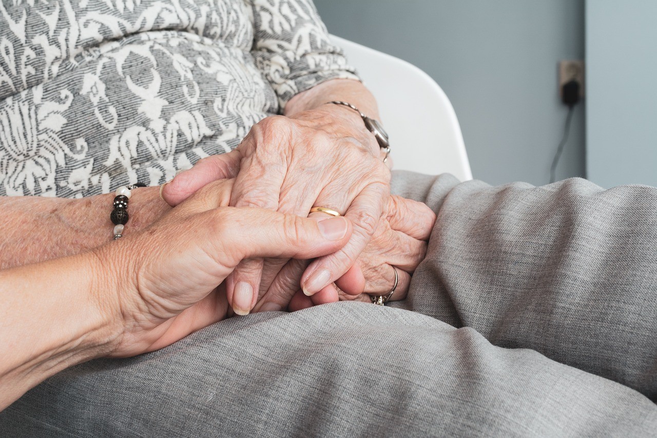 Zwei Hände halten sich am Krankenbett